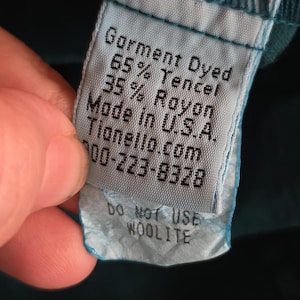 May include: A close-up of a teal garment tag with the text "Garment Dyed, 65% Tencel, 35% Rayon, Made in U.S.A." and "Do Not Use Woolite". The tag is attached to a teal fabric.
