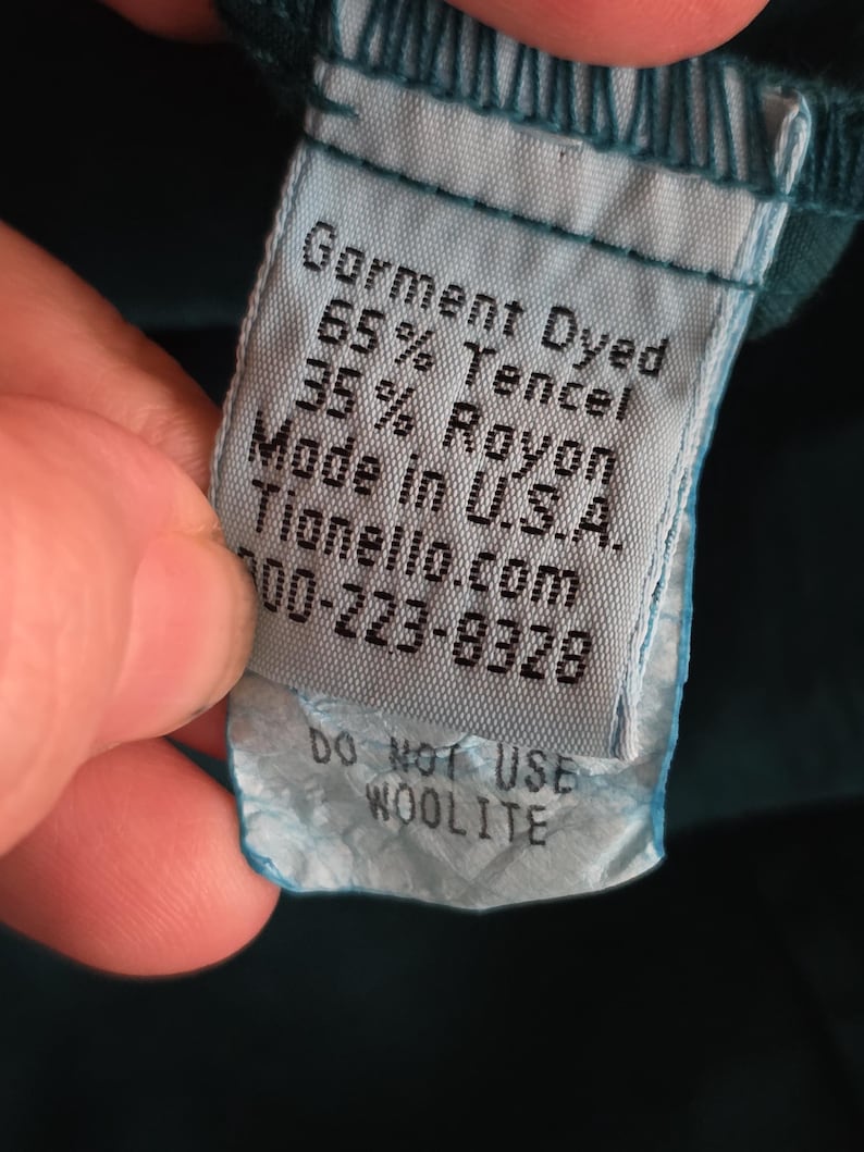 May include: A close-up of a teal garment tag with the text "Garment Dyed, 65% Tencel, 35% Rayon, Made in U.S.A." and "Do Not Use Woolite". The tag is attached to a teal fabric.