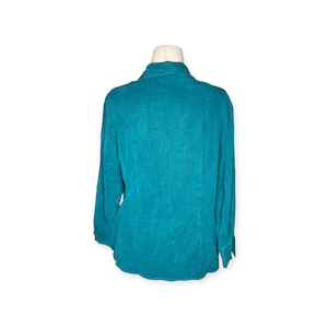 May include: Teal-colored long-sleeve button-down shirt. The shirt is displayed on a mannequin, showcasing the back of the garment. The fabric has a textured appearance, and the collar is visible.