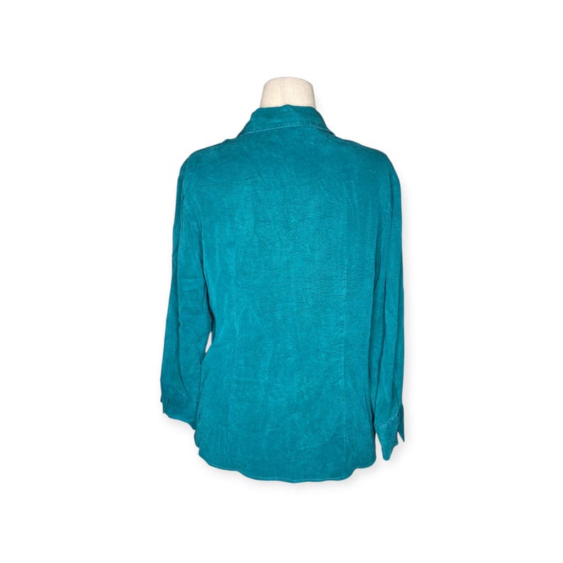 May include: Teal-colored long-sleeve button-down shirt. The shirt is displayed on a mannequin, showcasing the back of the garment. The fabric has a textured appearance, and the collar is visible.