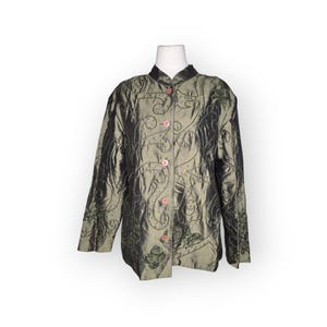 May include: Olive green jacket with a mandarin collar and long sleeves. The jacket features embroidered floral and swirl designs, accented with small green beads. It has pink buttons down the front and is displayed on a mannequin.