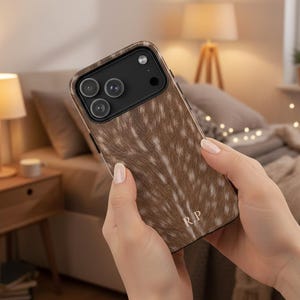 Puede incluir: Una funda de teléfono con estampado marrón y blanco con las iniciales "R.P." se sostiene en las manos de una persona. La funda tiene un aspecto texturizado, que se asemeja a la piel de un animal. La funda del teléfono tiene un módulo de cámara negro.