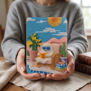 May include: A beaded case featuring a whimsical scene of a ghost in sunglasses reading a book while relaxing in a chair. The case has a blue sky, sun, and cactus design. The case is held in a person's hands.