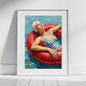 Puede incluir: Impresión de pintura al óleo de una mujer con un bañador a rayas azules y blancas y un gorro de baño blanco, flotando en un flotador rojo en el agua. La obra de arte está enmarcada en un marco blanco.