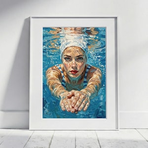 Op de afbeelding: Een ingelijste kunstdruk van een vrouw die onder water zwemt. Ze draagt een witte badmuts en een blauw-wit gestreepte zwemkleding. Het kunstwerk is geschilderd in blauwtinten en toont het gezicht en de armen van de zwemster.