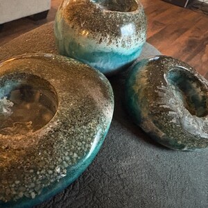 May include: Three decorative resin pieces in shades of teal, brown, and clear. The pieces include two oval-shaped candle holders and a small round vase. The resin has a textured, speckled appearance, creating a unique aesthetic.