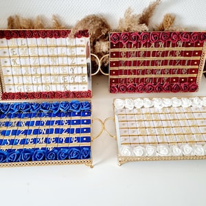 May include: Four gold trays with white chocolate bars decorated with gold lettering. Each tray is lined with a different color of fabric and flowers. The trays spell out the words "ALLAHIN", "EMRIYLE", "KIZINIZ", "ISTE MEYE GELDIK".