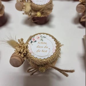 Peut inclure: Un petit pot en verre avec un couvercle en toile de jute et un autocollant décoratif qui dit "Schön, dass du da bist". Le pot est attaché avec de la ficelle et a un petit bâtonnet de miel en bois attaché.