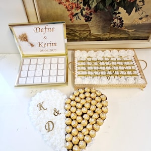 May include: A collection of wedding favors, including a gold-framed box with chocolates and the names "Defne & Kerim" and the date "08.06.2025". A tray with chocolates and the text "EMRİYLE KIZINIZI İSTEMEYE". A heart-shaped arrangement with white flowers and chocolates.