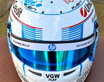 Könnte beinhalten: Ein weißer Rennhelm mit blauen Grafikmustern, dem Monaco Grand Prix Logo und verschiedenen Sponsorenaufklebern wie UniCredit, HP, Richard Mille, VGW Play, Shell V-Power und VistaJet. Der Helm verfügt über ein reflektierendes blaues Visier.