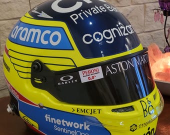 May include: A yellow, blue, and black racing helmet with sponsor logos, including "aramco," "cognizant," and "Aston Martin." The helmet features a dark visor and the text "finetwork SentinelOne."