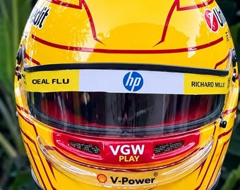 Könnte beinhalten: Ein leuchtend gelber Rennhelm mit roten grafischen Akzenten und verschiedenen Sponsorenlogos wie HP, VGW Play, V-Power und Vista Jet. Der Helm verfügt über ein klares Visier, eine Kinnbelüftung und schwarze Beschläge an den Seiten.
