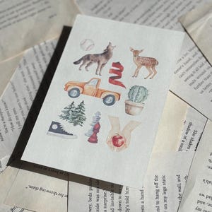 May include: A watercolor sticker sheet featuring various illustrations, including a howling wolf, a deer, an orange pickup truck, a baseball, a cactus, a pine tree, a high-top sneaker, a chess piece, and a hand holding an apple.
