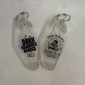 May include: Two clear, glitter-filled keychains with silver key rings. One keychain reads "Dark Romance Reader" with a book graphic. The other says "Dark Romance Readers Book Club" with a skull and book graphic.
