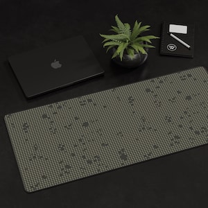 Peut inclure: Un ordinateur portable noir avec un tapis de souris à motifs vert et noir sur une surface noire. Une plante verte en pot et un carnet noir avec un stylo blanc sont également sur la surface.
