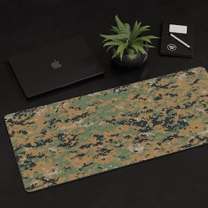 K&ouml;nnte beinhalten: Eine gro&szlig;e, rechteckige Mausmatte mit einem digitalen Tarnmuster in Gr&uuml;n-, Braun- und Beiget&ouml;nen. Die Mausmatte liegt auf einer schwarzen Oberfl&auml;che.