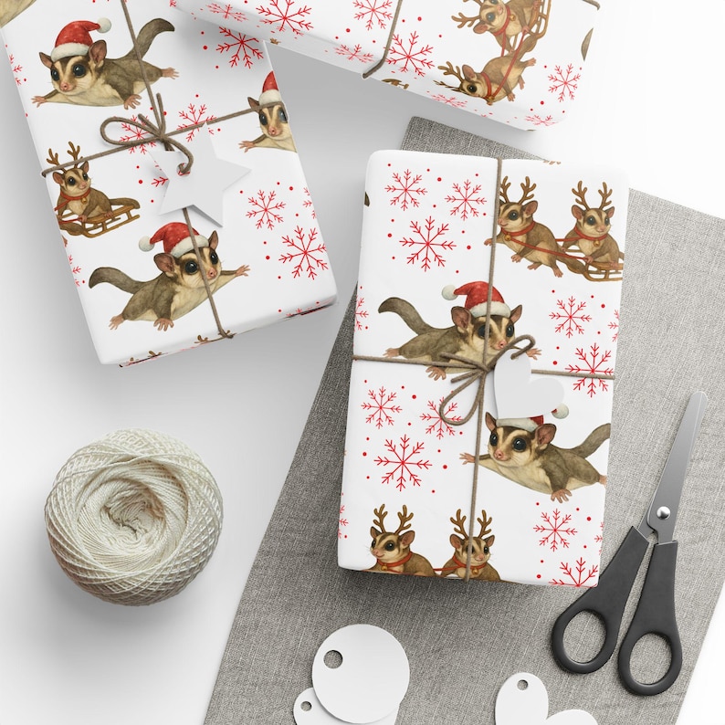 May include: Wrapped gifts with a festive Christmas theme. The white wrapping paper features a repeating pattern of sugar gliders wearing Santa hats and reindeer pulling a sled, along with red snowflakes. Tied with twine and a star-shaped tag.