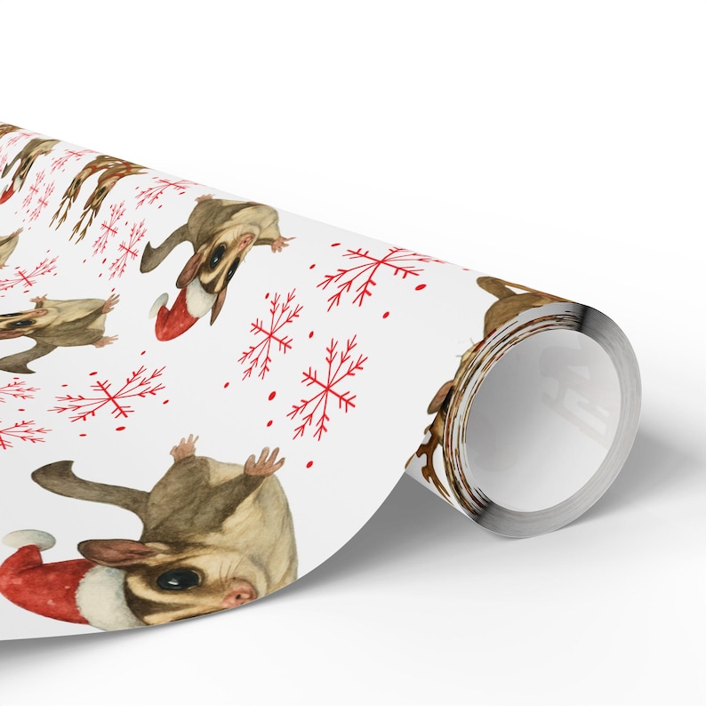 May include: White wrapping paper featuring a repeating pattern of sugar gliders wearing Santa hats and red snowflakes. The paper is rolled up, showing the design on the front.