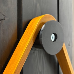 May include: A wooden wall mount for pool cues, featuring a black circular base with a screw in the center. The mount is made of two pieces of wood that form a triangle shape.