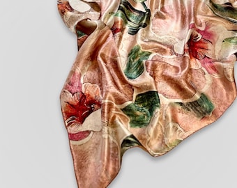 May include: A brown silk scarf with a floral print featuring large pink and red flowers with green leaves. The scarf is draped and folded on a white background.