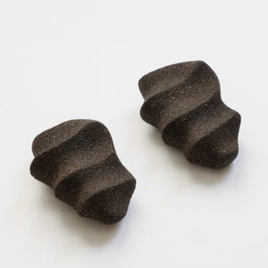 May include: Two dark brown, textured ceramic objects with a unique, twisted design. The objects have a rough, speckled surface and a series of horizontal ridges. They are set against a plain white background.