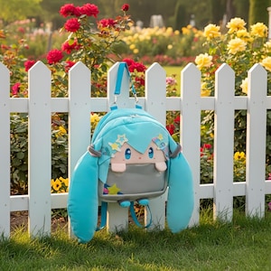 Puede incluir: Una mochila azul claro con un diseño de personaje de dibujos animados, con pelo largo y fluido de color turquesa y detalles de estrellas. La mochila tiene un bolsillo gris y está colgada de una valla blanca frente a un jardín con rosas rojas y amarillas.