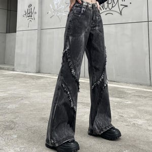 May include: High-waisted denim jeans in a washed-out charcoal gray with a distressed acid-wash effect. The pants feature wide legs and prominent vertical seams down the front of each leg, accented with raw, frayed edges along the seam lines.