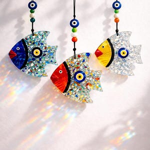 Pu&ograve; includere: Tre ornamenti decorativi a forma di pesce con motivi a mosaico. Ogni pesce presenta una diversa combinazione di colori: blu, rosso e giallo. Sono decorati con un occhio turco e appesi a cordoncini neri, adatti per l'arredamento della casa.