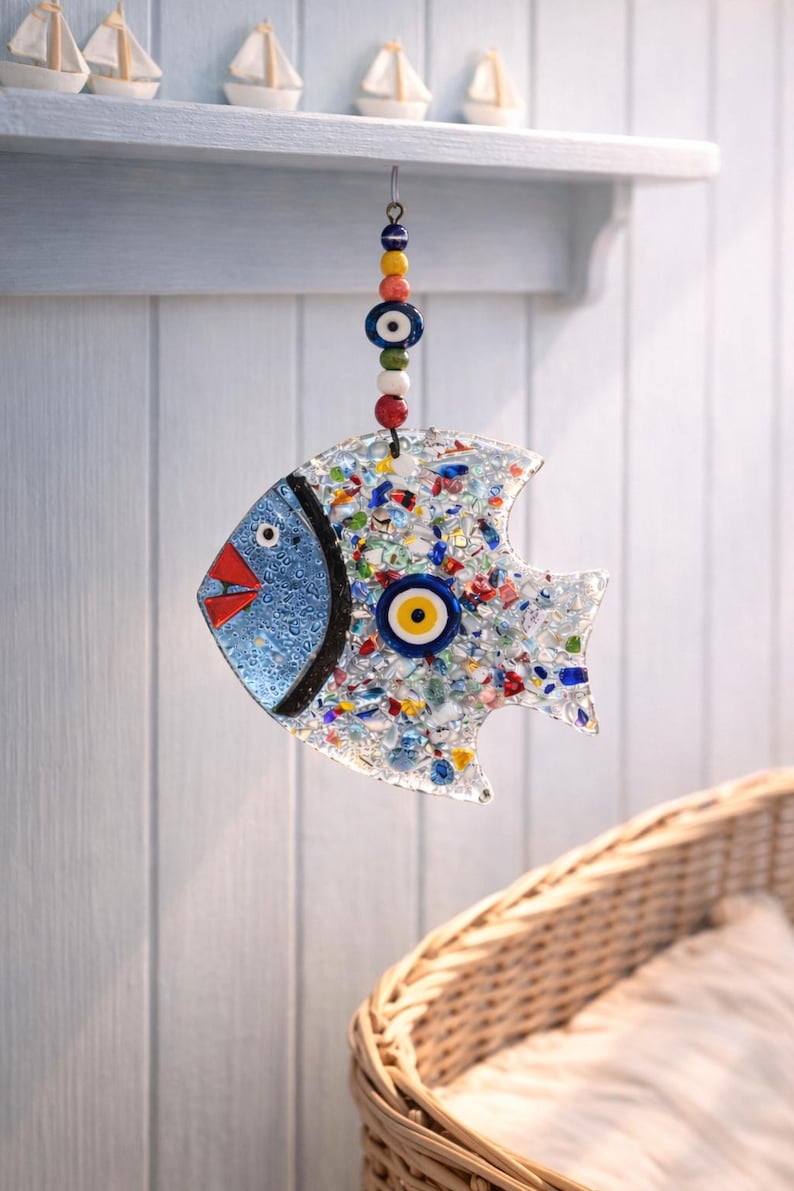 Pu&ograve; includere: Un ornamento decorativo a forma di pesce con testa blu, bocca rossa e corpo pieno di pezzi di vetro colorati. Presenta un ciondolo a forma di occhio e viene sospeso da una corda di perline. Misura circa 15 cm di lunghezza.