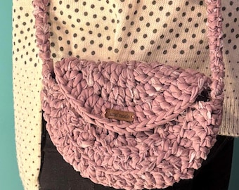 May include: A mauve crocheted bag with a brown leather tag that says "hand made".