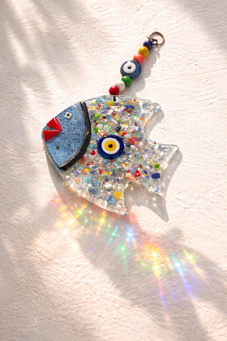 Pu&ograve; includere: Un ornamento decorativo a forma di pesce con testa blu, labbra rosse e corpo pieno di pezzi di vetro colorati. Presenta un ciondolo a forma di occhio e una catena di perline per appenderlo. L'ornamento &egrave; lungo circa 13 cm.