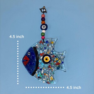 A decorative glass fish, 4.5 inches in length, with a blue body and mosaic-style design. The fish features a blue eye, red beak, and a yellow and black eye. It hangs from a beaded strand with colorful beads.