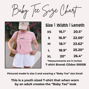 May include: A pink baby tee size chart with measurements in inches. The chart includes sizes XS to XL, with width and length measurements. The model is wearing a size small. The shirt is a youth size that creates a baby tee look.