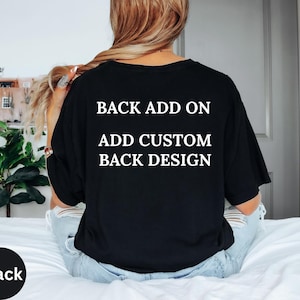Peut inclure: T-shirt noir avec texte blanc : "BACK ADD ON ADD CUSTOM BACK DESIGN". Un cercle noir avec le mot "Black" est en bas à gauche. Le t-shirt est porté par une personne assise sur un lit.