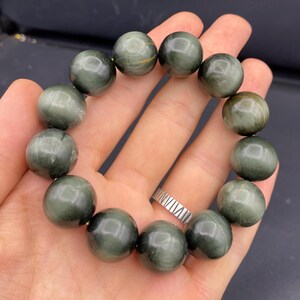May include: A bracelet featuring large, round beads in shades of green and gray. The beads have a polished, glossy finish and are strung together to form a circular shape. The bracelet is shown resting on a hand.
