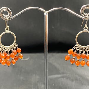 Può includere: Orecchini a cerchio d'argento con un gruppo di perle di cornalina arancione pendenti.