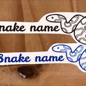 May include: Two white stickers with the text "Snake name" in black and blue lettering. Each sticker features a black and blue outline of a snake with a patterned body.
