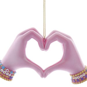 May include: A pink ornament shaped like hands forming a heart. The hands wear beaded bracelets with the word "LOVE" spelled out. The ornament hangs from a gold string, perfect for Valentine's Day or expressing affection.