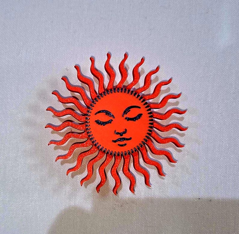 Puede incluir: Un dise&ntilde;o de sol de madera con una cara sonriente y ojos cerrados. El sol est&aacute; pintado de naranja con rayos ondulados y detalles negros. El sol mide aproximadamente 10 cm de di&aacute;metro.