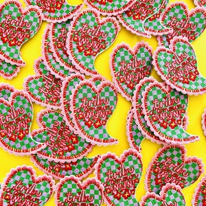 Op de afbeelding: Een verzameling roze en groene hartvormige patches met de tekst "tribu d'amour" en "infinix" erop geborduurd.