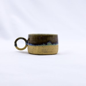 May include: A small, yellow ceramic mug with a brown and blue glaze. The mug has a rounded handle.