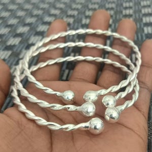 May include: Three silver twisted bangle bracelets with round ball accents.