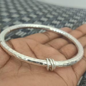 May include: A silver hammered bangle bracelet with a simple, rounded design. The bracelet is open and has a hammered texture.