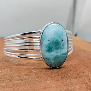 May include: A silver bangle bracelet with a large oval-shaped blue and green gemstone set in the center. The bracelet has a multi-strand design.