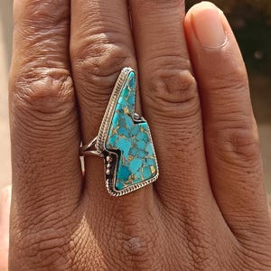 Puede incluir: Un anillo de plata con una piedra turquesa en forma de rayo.