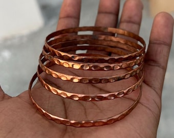 May include: A set of five copper bangles with a hammered texture. The bangles are stacked on top of each other and are a warm, reddish-brown color.
