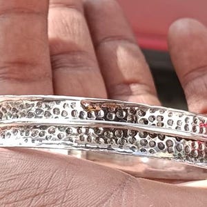 Könnte beinhalten: Ein silbernes Armband mit gehämmerter Textur und einem Doppelband-Design.