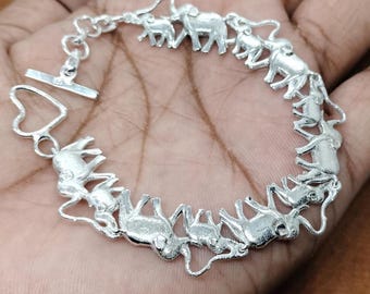 May include: A silver bracelet with a chain and a series of elephant charms. The elephants are all facing the same direction and are connected to the chain by their trunks.