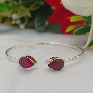 May include: A silver bangle bracelet with two teardrop-shaped pink gemstones.