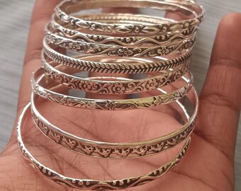 May include: A set of eight silver-toned bangles with intricate floral and geometric designs. The bangles are stacked on top of each other, creating a layered look.